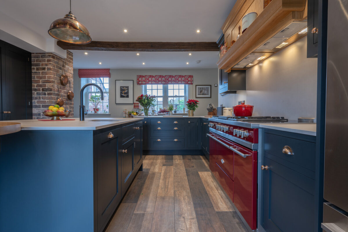 Handmade navy blue kitchen with red range cooker, wooden beam and brick feature wall in a characterful home interior