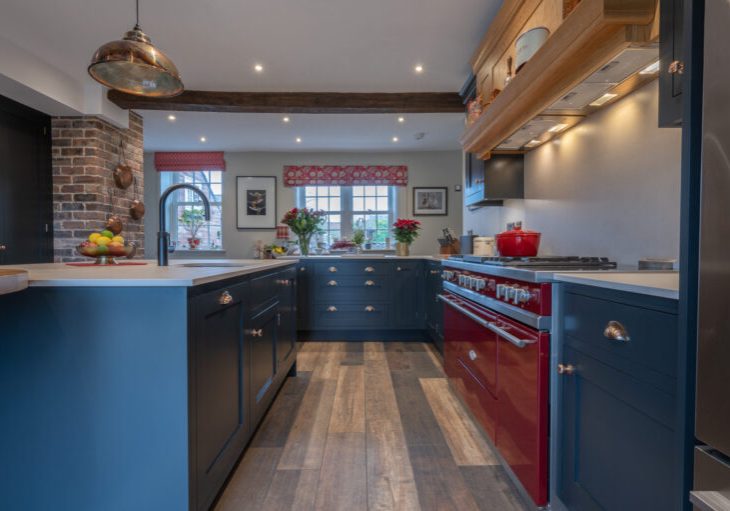 Handmade navy blue kitchen with red range cooker, wooden beam and brick feature wall in a characterful home interior